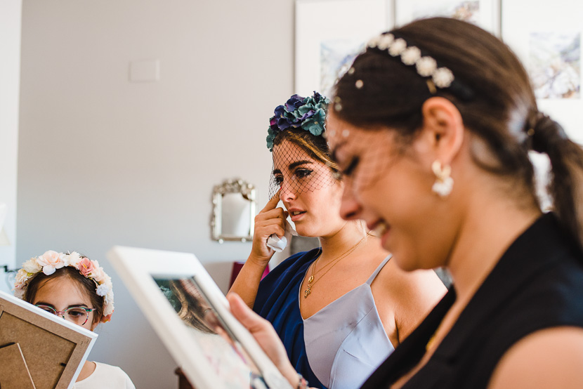 Dama de honor llorando en un momento emotivo al recibir un regalo de la novia durante los preparativos fotografiado por Bodas con Arte