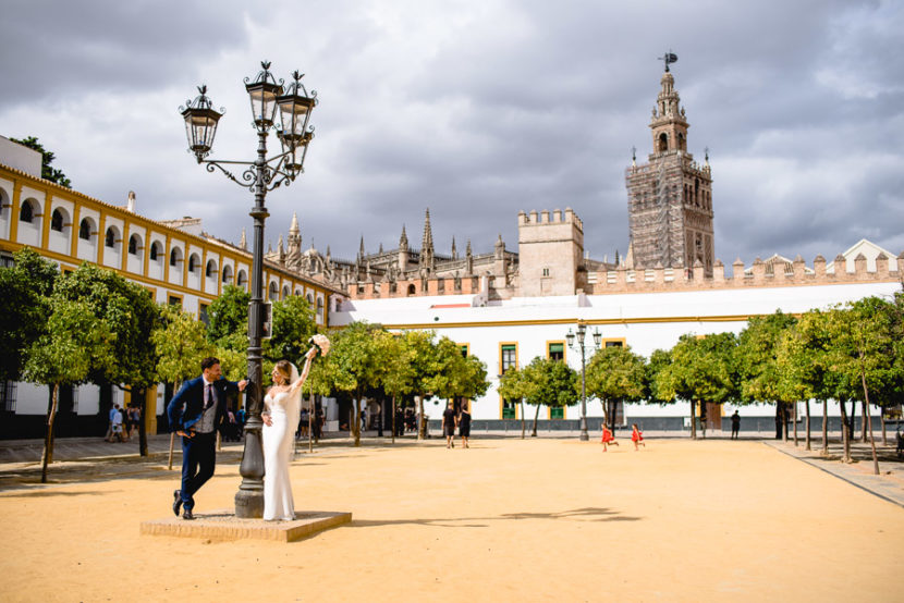 Pareja de recien casados posando en el patio de los naranjos con la Giralda de fondo. Foto por Bodas con Arte, Fotógrafos de bodas en Sevilla